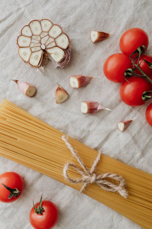 Free Flat lay of cherry tomatoes, garlic, and spaghetti on a rustic cloth. Stock Photo