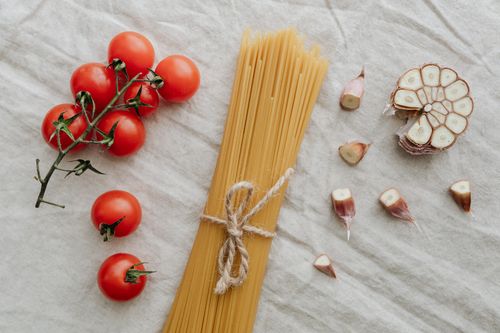 Free Flat lay of cherry tomatoes, garlic, and uncooked spaghetti on a neutral background. Ideal for food photography. Stock Photo
