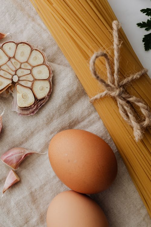 Free Fresh garlic, eggs, and uncooked spaghetti arranged on a cloth, perfect for pasta recipes. Stock Photo