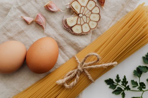Free Flat lay of raw spaghetti, garlic, and eggs on linen, showcasing fresh ingredients. Stock Photo