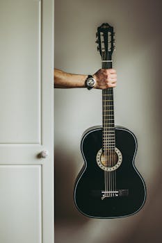 A hand holding an acoustic guitar indoors, offering a modern and artistic vibe.