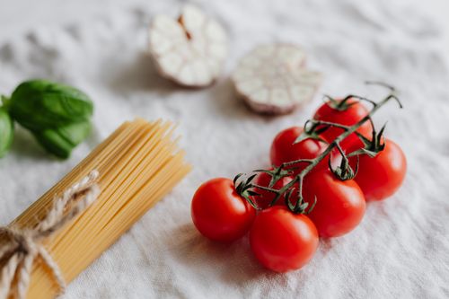 Free A close-up of cherry tomatoes and pasta with garlic and basil, ideal for culinary themes. Stock Photo
