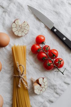 Top view of fresh pasta ingredients including garlic, tomatoes, and eggs on a white surface.