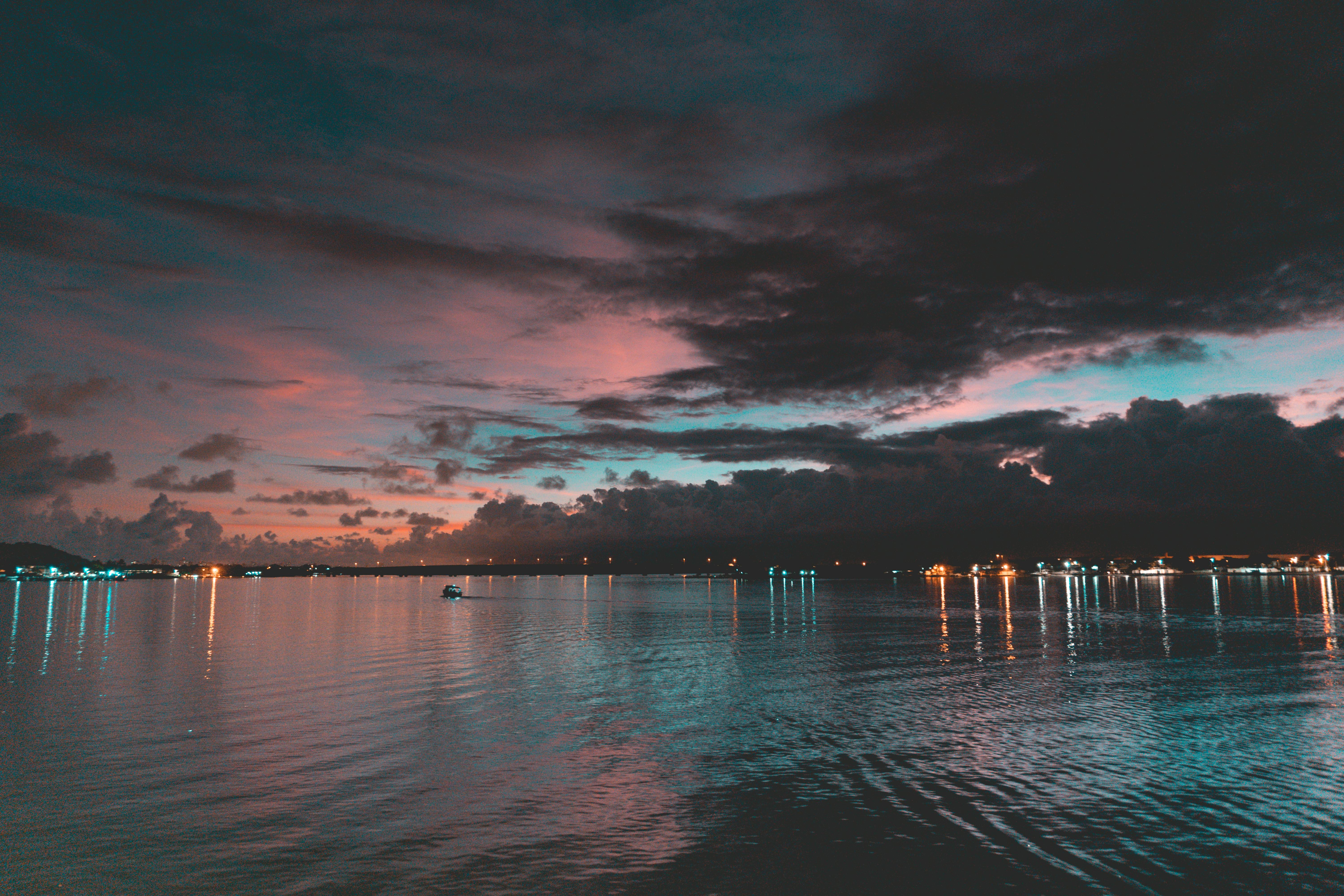 A beautiful seascape at twilight with vibrant sky reflections and lights along the shoreline.