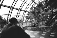 两名身穿休闲服、戴着帽子的匿名男子，一黑一白，在装饰着各种异国情调植物的舒适咖啡馆里休息