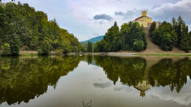 Scenic view of Trakoscan Castle reflecting in a serene lake surrounded by lush greenery.