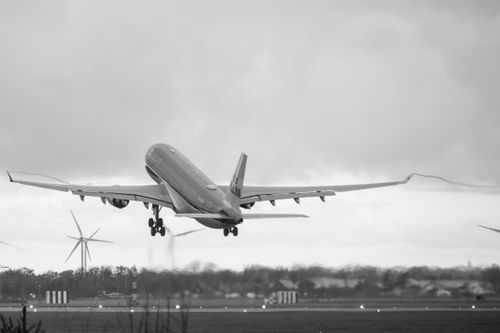 Free Dramatic black and white shot of a commercial airplane taking off with wind turbines in the background. Stock Photo