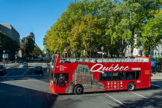 Double-decker tour bus on a street in Quebec City, showcasing urban landscape and greenery.