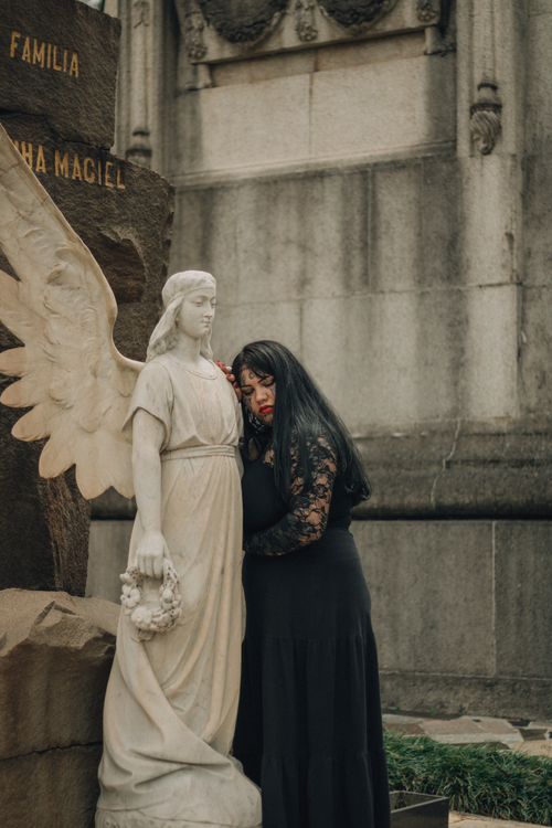 Free A woman in black embraces a marble angel statue in a cemetery, creating a somber and mystical atmosphere. Stock Photo