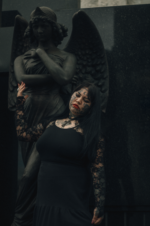 Free A woman in gothic attire poses beside a somber angel statue, evoking a dark, dramatic aesthetic. Stock Photo