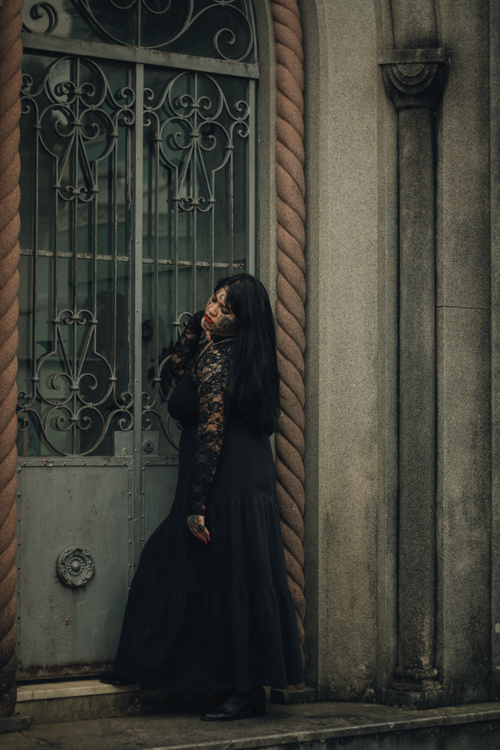 Free A woman in gothic attire leans on an ornate gate, exuding a mysterious and dramatic appearance. Stock Photo