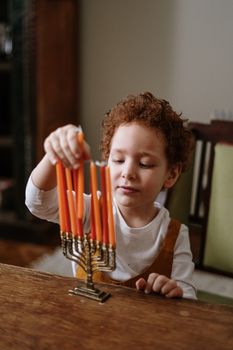 一个红发卷毛的幼童，在室内点亮了光明节的烛光