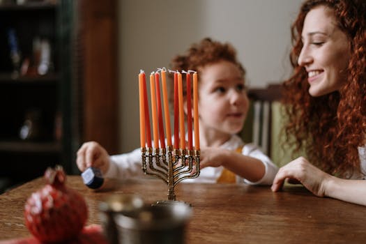 A mother and child celebrate Hanukkah indoors with a menorah and dreidel.