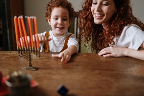 Free A joyful mother and son lighting a menorah during Hanukkah at their cozy home. Stock Photo