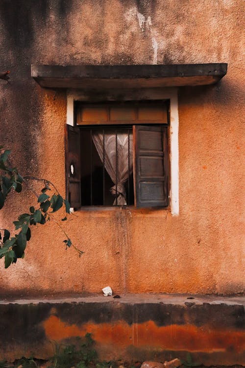 Exterior of aged concrete orange house with weathered wall and opened wooden window