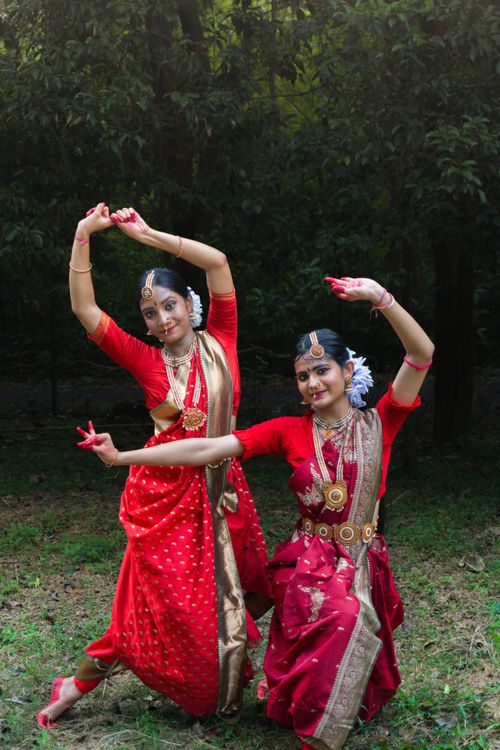 Free Two women in vibrant red sarees perform a classical Indian dance outdoors. Stock Photo