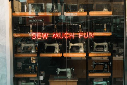 Free Showcase of antique sewing machines with a neon sign saying 'Sew Much Fun'. Stock Photo