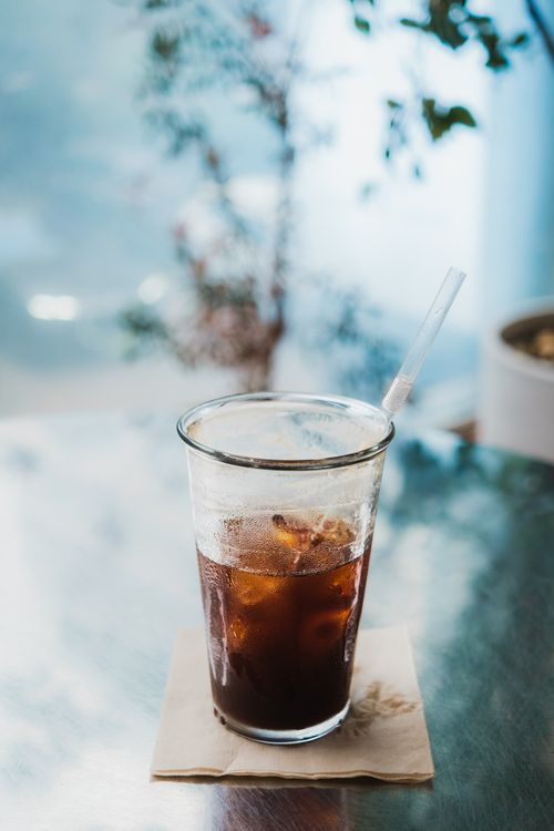 Free Glass of iced coffee with straw on a metallic table in a bright cafe. Stock Photo