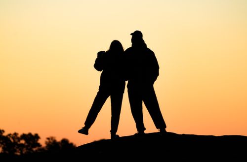 Free Silhouette of two people standing on a hill against a vibrant sunset sky. Stock Photo