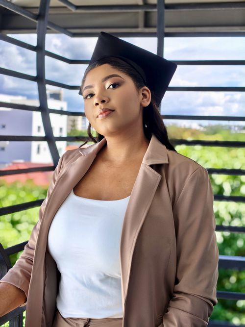 Free A young woman wearing a graduation cap confidently poses outdoors with city and greenery in the background. Stock Photo