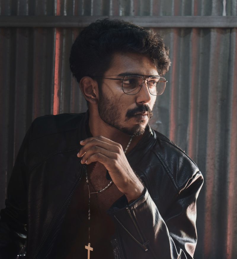 Portrait of a stylish man wearing glasses and a leather jacket with serious expression.