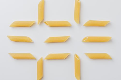 Free Array of uncooked penne pasta on a white background in a minimalist style. Stock Photo
