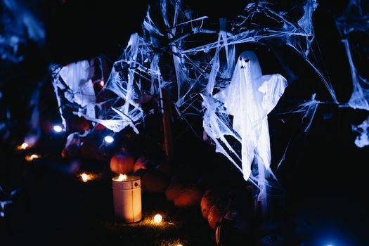 Eerie Halloween scene with ghost decorations and pumpkins illuminated in blue light.