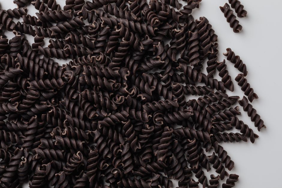 Top view of uncooked black fusilli pasta spirals on a white surface.