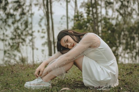 身着白色连衣裙和运动鞋的年轻民族女士在绿色森林的草地上放松的侧视图