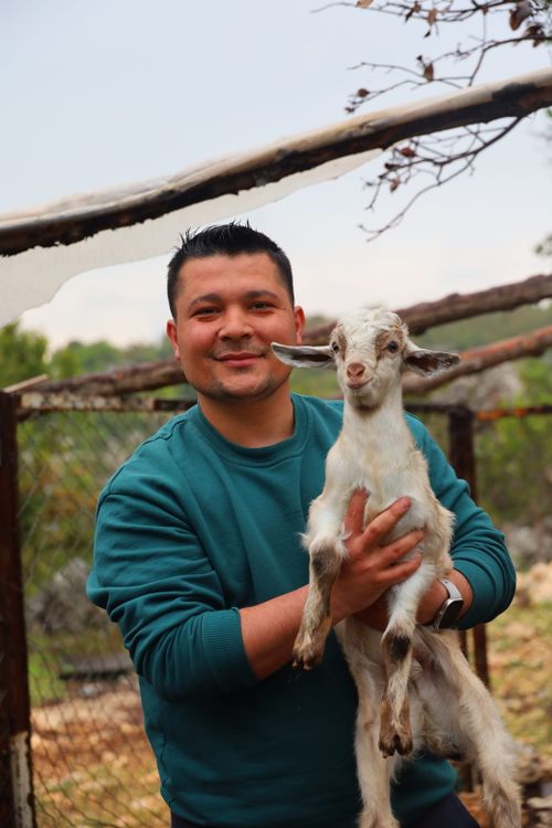 Free A smiling man poses with a cute baby goat in an outdoor setting. Stock Photo