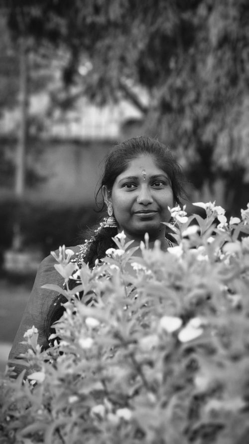 Free Black and white portrait of a woman behind flowering plants in a garden. Stock Photo