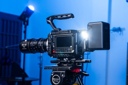 Free Close-up of a professional video camera on a tripod in a studio setting with blue lighting. Stock Photo