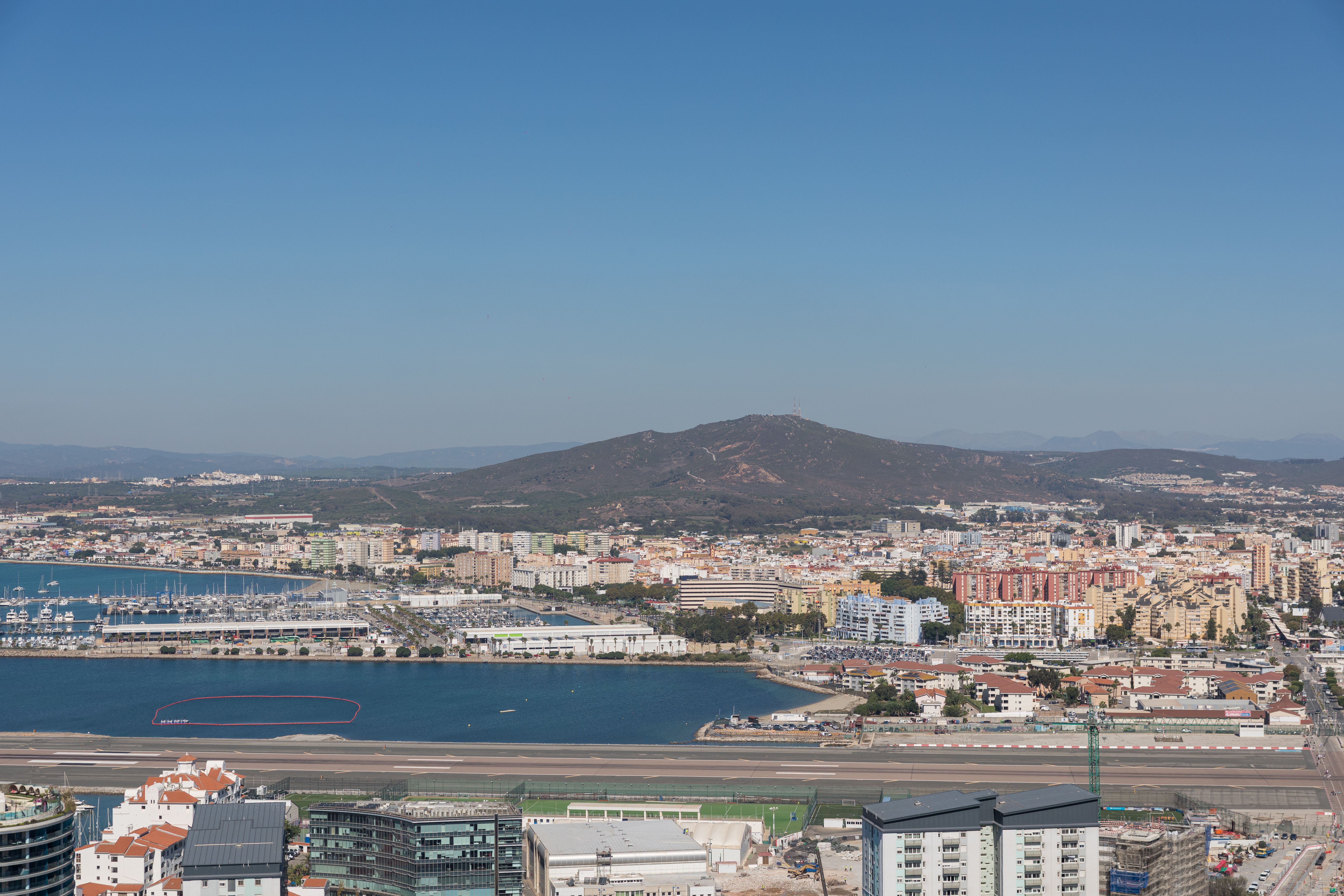 Fotomural Impresionante vista aérea de Gibraltar con su pintoresco paisaje urbano, bahía y colinas circundantes bajo un cielo azul despejado.