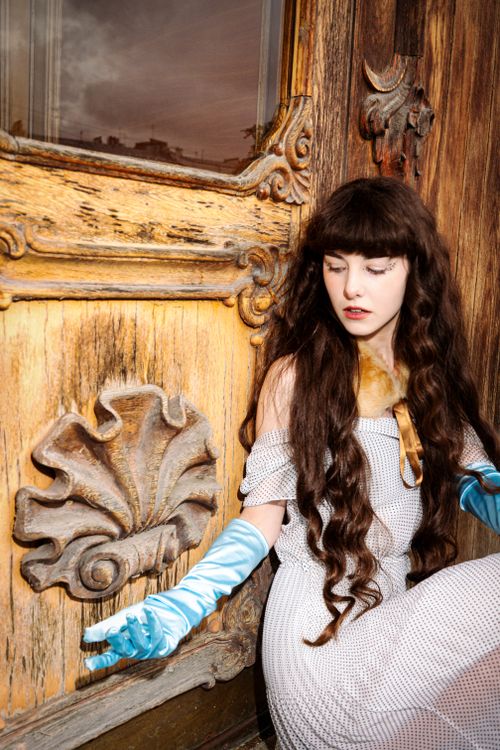 Free A woman in a vintage gown with long hair and gloves posed by an ornate wooden door. Stock Photo