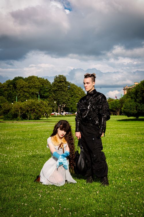 Free A stylish duo poses in unique fashion outfits on a lush green lawn under a dramatic sky. Stock Photo