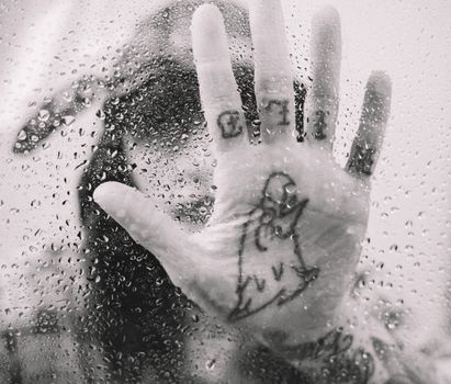 透过玻璃，黑色和白色的手掌与雨滴玻璃上匿名者的纹身交织在一起
