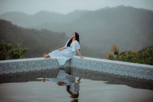 Woman in white dress enjoys tranquil moment by infinity pool with mountain view.