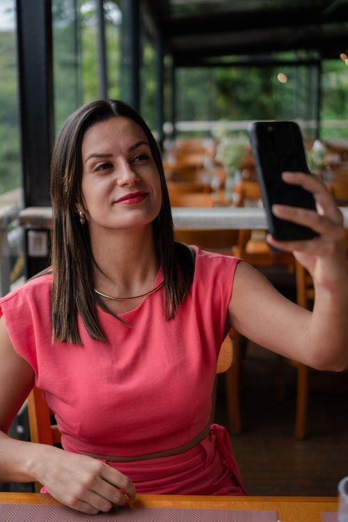 Free A young woman in a pink dress takes a selfie inside a cafe with a scenic view. Stock Photo
