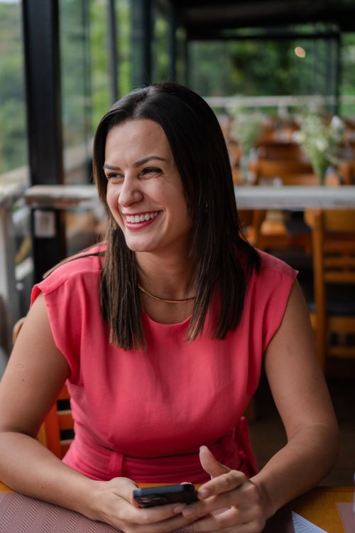 Free A cheerful woman seated indoors in a cafe, holding a phone and smiling brightly. Stock Photo