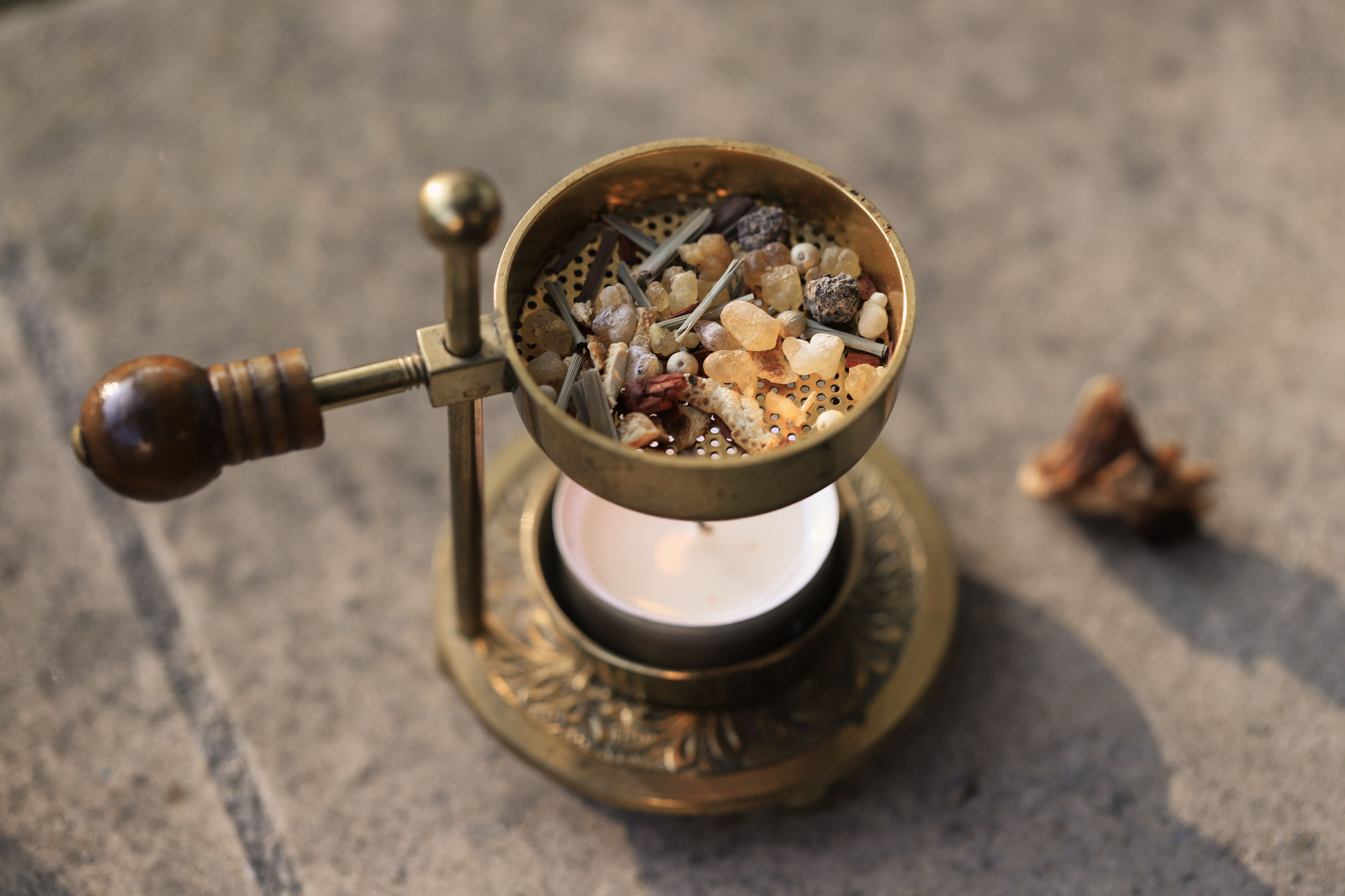 A brass incense burner with resin and herbs lit by a candle, perfect for meditation.