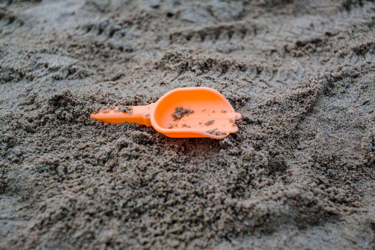 An orange plastic scoop lying on damp sand