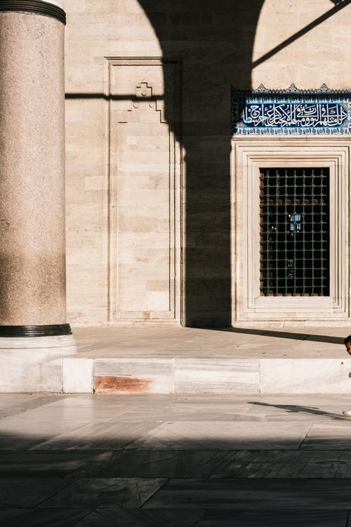 Free A serene sunlit courtyard with traditional architecture showcasing elegant pillars and an ornate window grille. Stock Photo