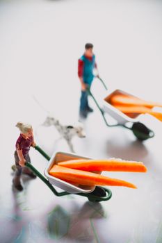 High angle of toys for children in shape of man and woman in uniform carrying wheelbarrow with orange sticks