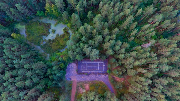 Drone shot of a secluded tennis court surrounded by lush green forest in Varėna, Lithuania.