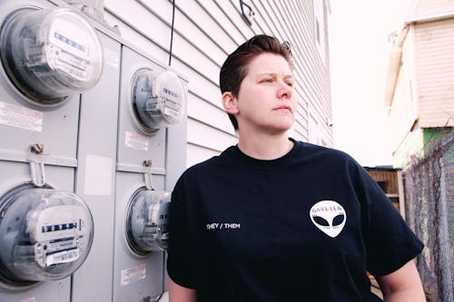 Photo of a Woman in a Black Shirt Leaning on Electrical Meters