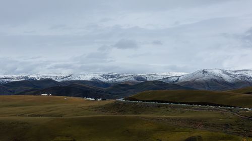 Free Beautiful expansive view of snow-capped mountains and vast green plains under a cloudy sky. Stock Photo