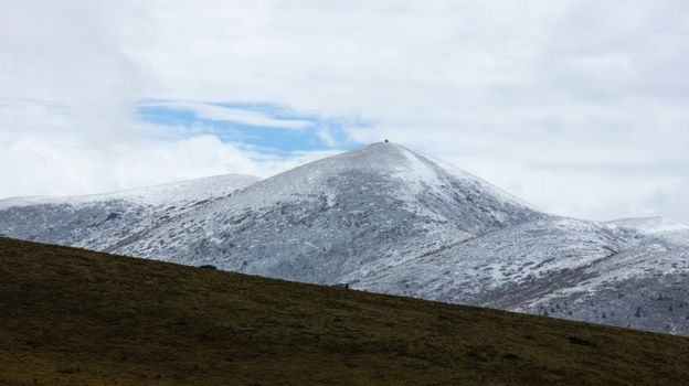 Serene snowy mountains and grassland under a bright cloudy sky.