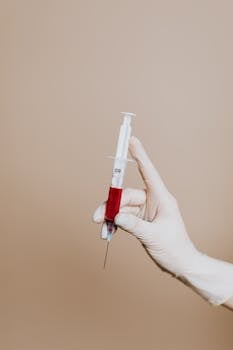 Close-up of a gloved hand holding a syringe filled with red liquid, symbolizing medical treatment or vaccination.