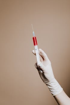 一只戴着手套的手握着注射器，置于中性背景下，突出了医学主题