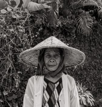巴厘岛一位老妇人的黑白肖像，她戴着传统帽子，背景是郁郁葱葱的自然景色。 - 相关推荐